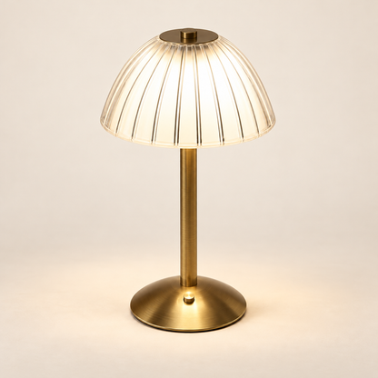 Cove rechargeable reading lamp in gold with a clear fluted acrylic shade on a warm ivory background