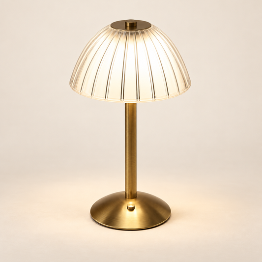 Cove rechargeable reading lamp in gold with a clear fluted acrylic shade on a warm ivory background
