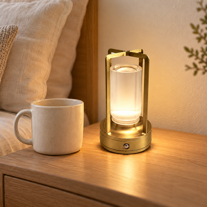 Noelle gold rechargeable table lamp beside an ivory mug on a warm bedside table, shown at scale.